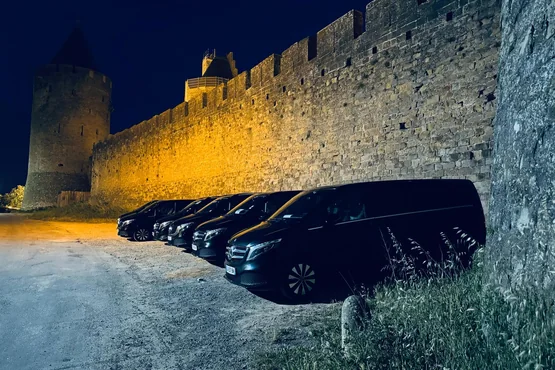 Van noir de Centrale VTC Toulouse stationné le soir devant des remparts illuminés.