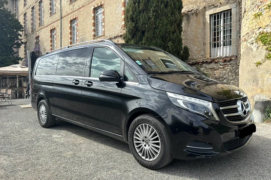 Van Mercedes noir stationné devant un bâtiment ancien en pierre, photographié de trois quarts avant.