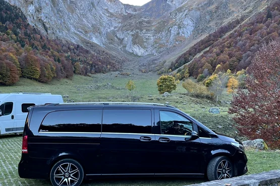 Van noir stationné au pied d’un paysage de montagne, derrière une barrière en bois.