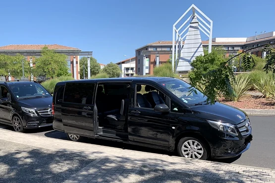 Plusieurs vans noirs stationnés devant des bâtiments, dont un van au premier plan avec sa porte latérale ouverte.